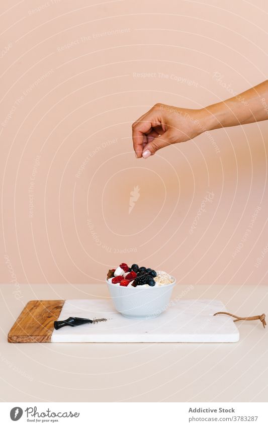 Crop woman adding coconut flakes in breakfast bowl sweet yogurt berry female table kitchen morning yummy fresh delicious tasty dessert muesli various assorted