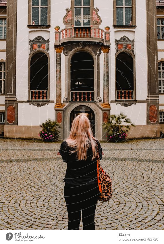 Young woman stands in front of the castle Füssen Sightseeing feet Bavaria Athletic back view Blonde long hairs fashionable traditon Lock Entrance Museum Culture