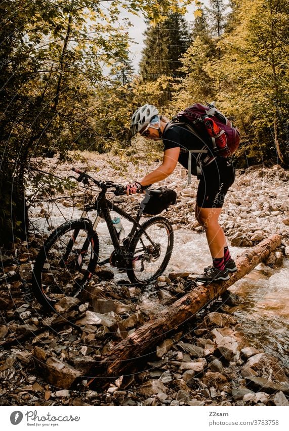 Young woman crosses river creek with her mountain bike Mountain bike mtb Bicycle Adventure Brook River Traverse Push stones Forest Alps mountains Nature