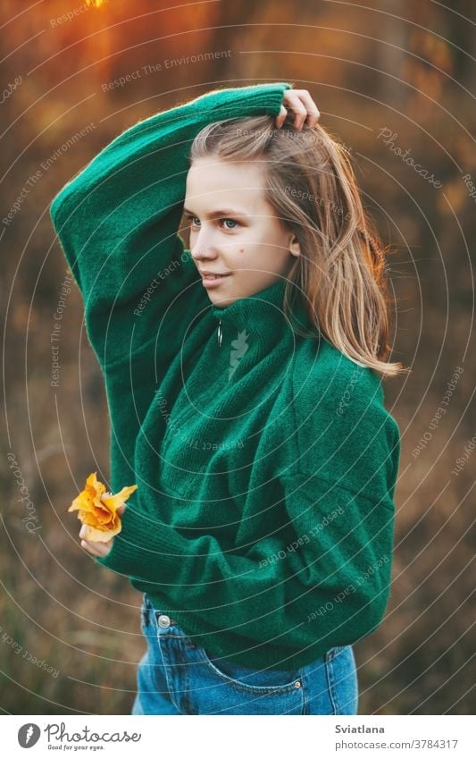 Portrait of a beautiful teenage girl with blond hair and blue eyes with a smile on her face and an autumn yellow leaf in the park. happy blonde portrait fall