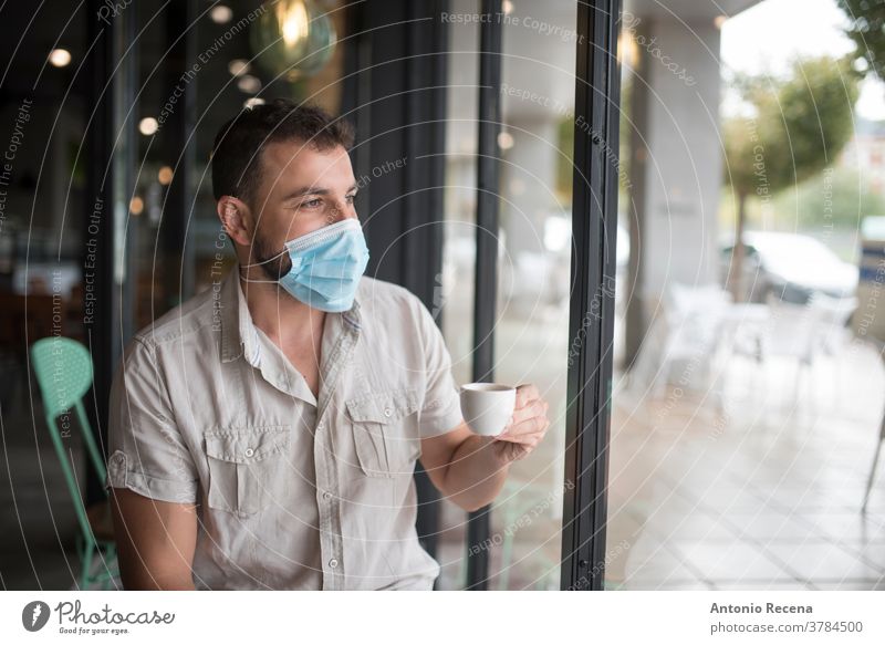 Man with surgical mask drinks coffee and looks out the window face covid-19 coronavirus pollution allergy person people one person protective corona virus