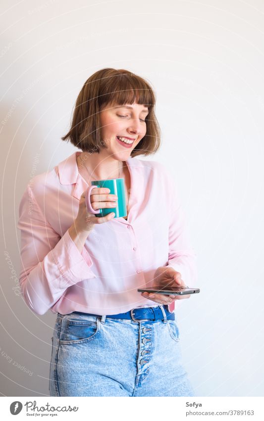 Woman drinking coffee and using smartphone woman device social media texting mobile phone smiling cup pink modern young positive optimist excited communication