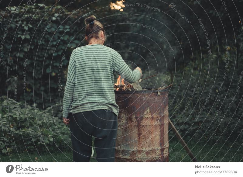 burning old branches barrel woman Human being Adults fire Colour photo Light Exterior shot Warmth metal barrel garden trees bush Nature Burn