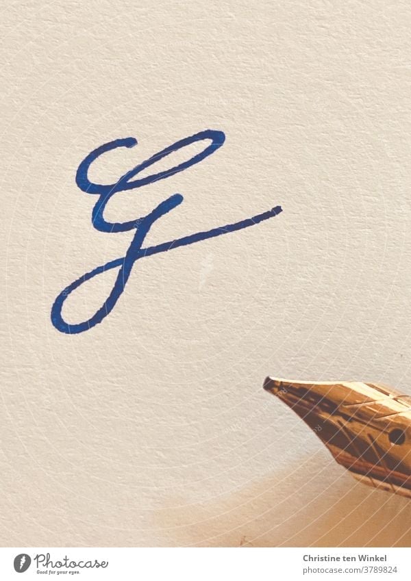 the squiggly letter G on light structured paper, written with blue ink. On the right edge of the picture you can see the golden tip of the fountain pen