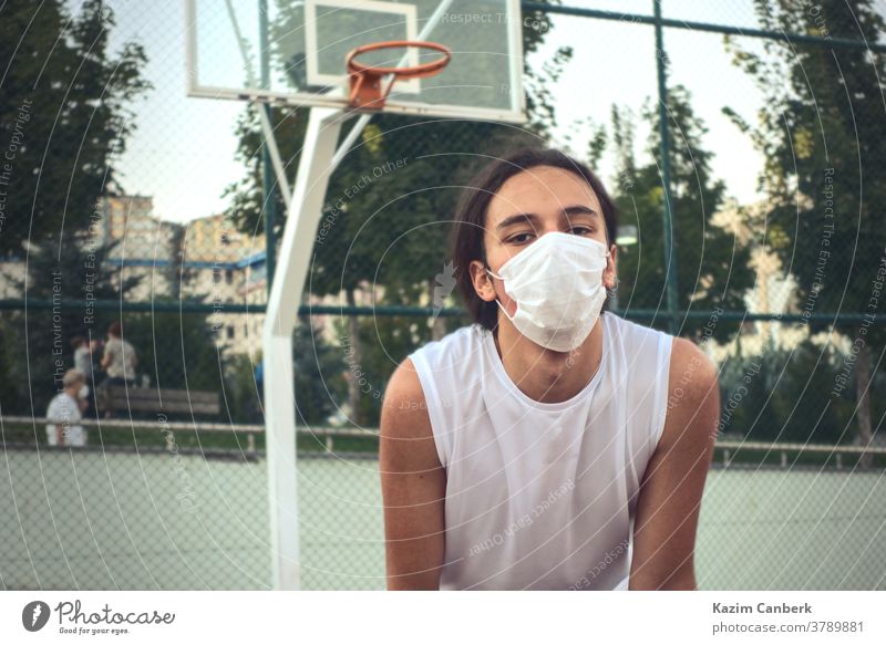 Teenager wearing a protective mask resting in front of basketball hoop young male man sport outdoor net tired masked handsome Authentic Basketball player