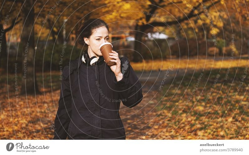 young woman drinking coffee to go while on the move take out lifestyle people outdoor candid real people autumn fall hot beverage disposable cup walking park