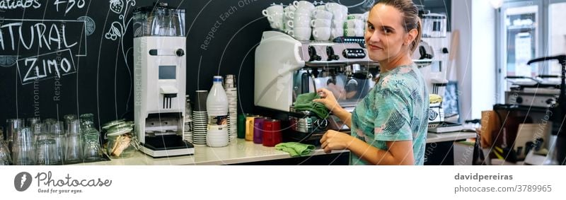 Smiling waitress cleaning coffee maker coffee machine coffee shop looking camera smiling banner header web panorama panoramic dishcloth restaurant cafeteria