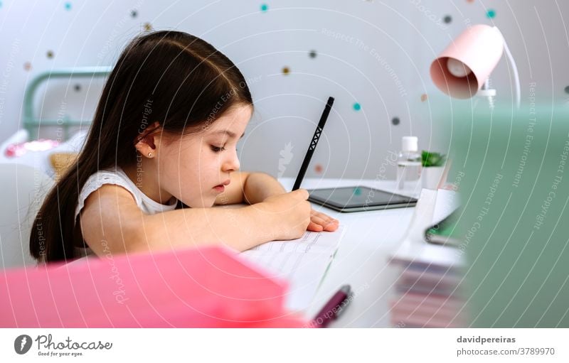 Girl doing homework sitting at a desk girl writing homeschooling school at home quiet wrong pencil posture closeup bedroom covid-19 online child beautiful cute