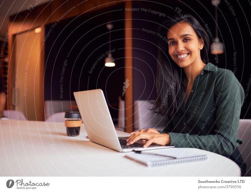 Portrait Of Businesswoman Sitting At Meeting Table Working On Laptop In Modern Open Plan Office business businesswomen meeting office sitting boardroom table