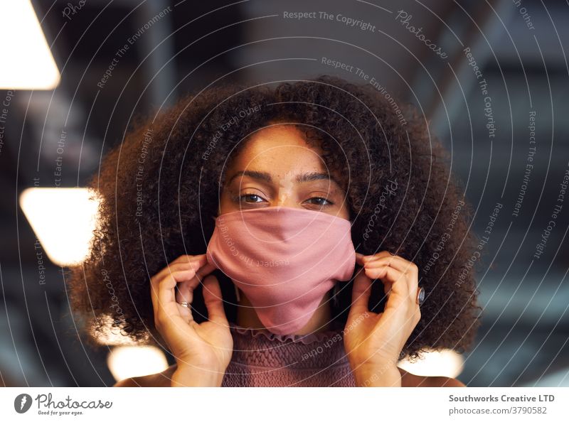 Portrait Of Businesswoman Putting On Face Mask In Modern Open Plan Office During Covid-19 Pandemic business businesswoman face mask face covering ppe putting on