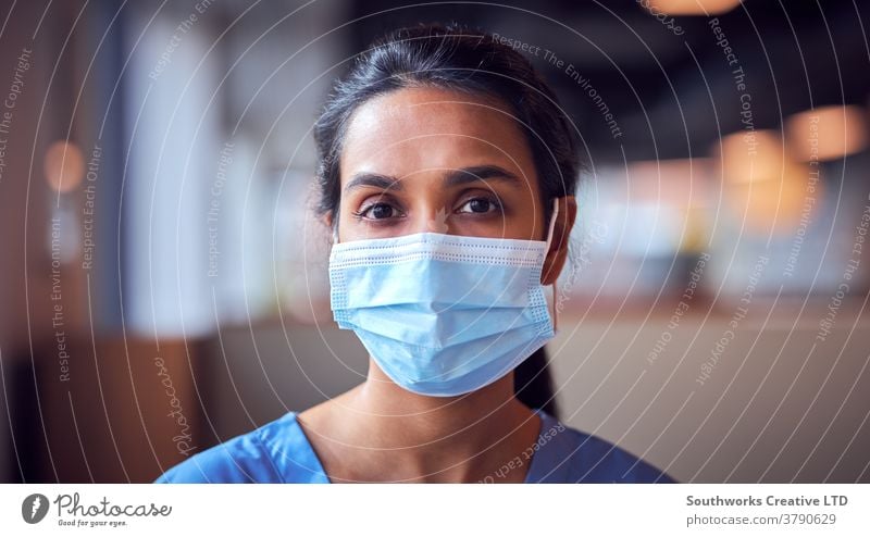 Female Doctor In Face Mask Wearing Scrubs Under Pressure In Busy Hospital During Health Pandemic doctor nurse scrubs key worker female woman wearing face mask