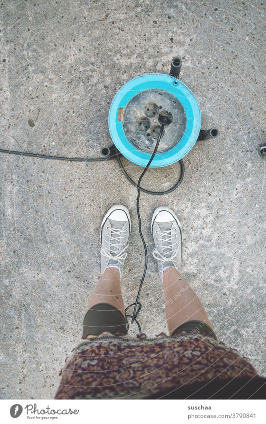 cable drum with power connection on asphalt, beside it the legs of a female person power supply portable Power plug power cable Connection Socket Cable