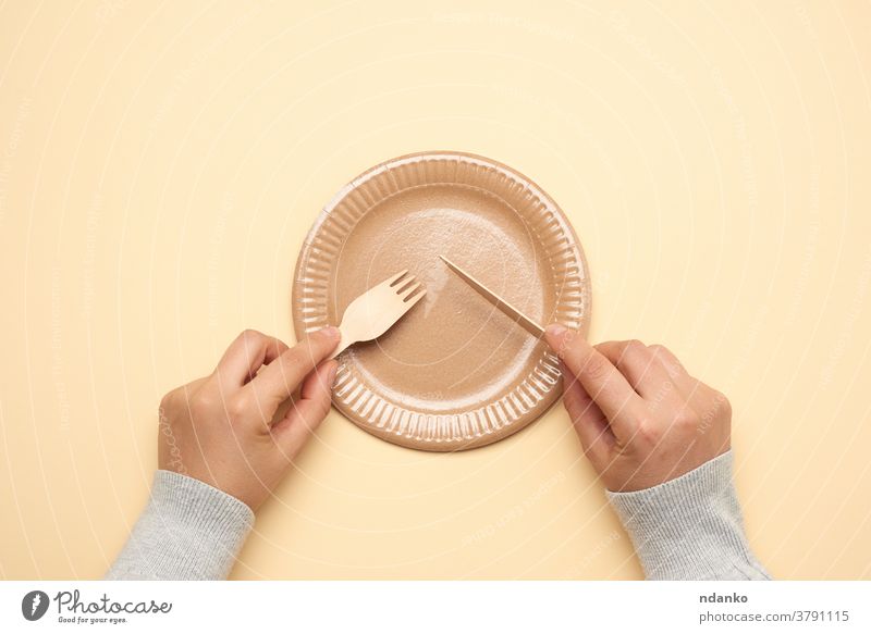 empty white paper plate and female hands are holding disposable fork and knife on beige background picnic recycle restaurant studio tableware template thick top