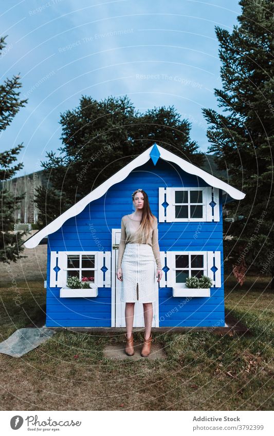 Attractive woman standing near small blue house confident cool style appearance trendy park calm construction emotionless tranquil gorgeous serene elegant