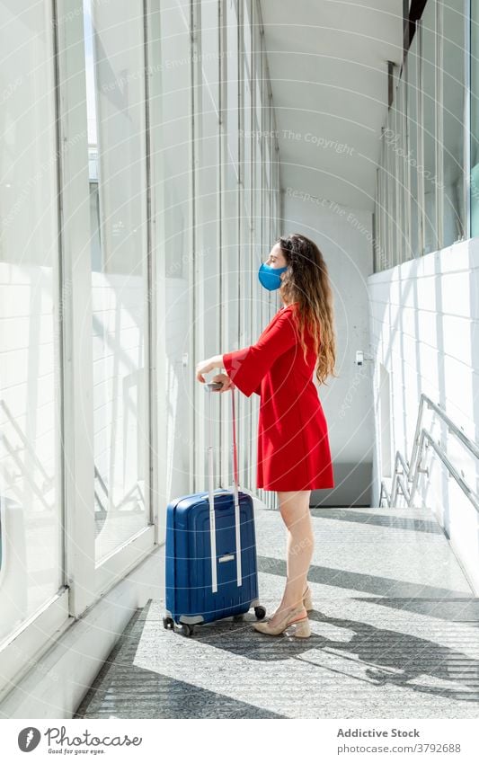 Traveling woman with baggage in airport travel wait flight departure suitcase mask coronavirus female tourist passenger vacation holiday window trip journey