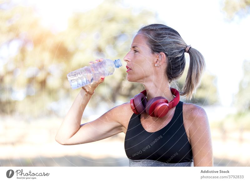 Slim sportswoman drinking water in park athlete training slender refreshment break sporty female bottle relax slim fit wellbeing sunny hydrate vitality beverage