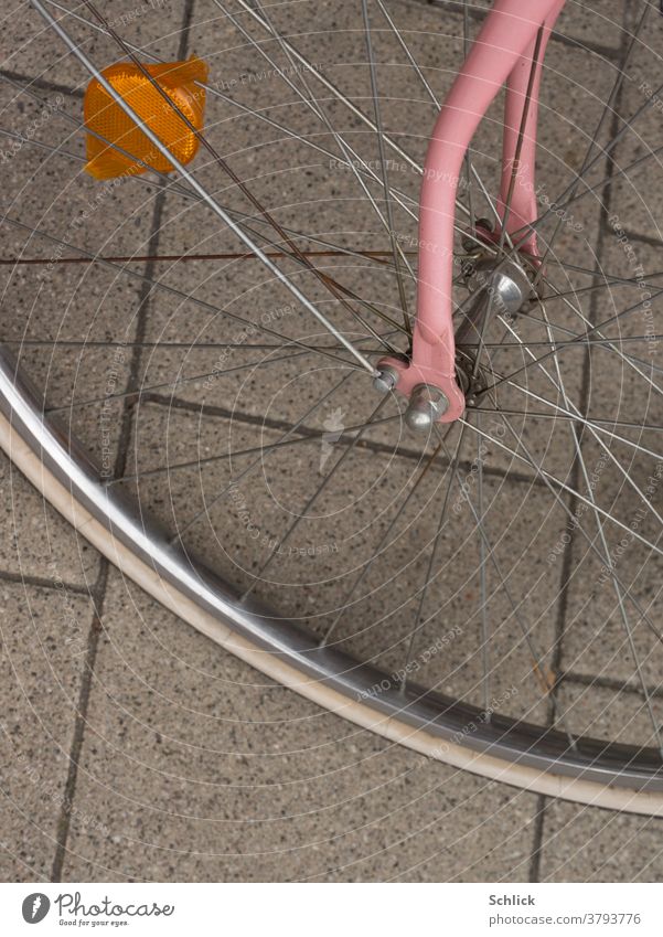 Detail of a bicycle front wheel with pink fork and orange reflector Bicycle Front wheel Fork Pink Reflector Bird's-eye view Orange concrete paving Old