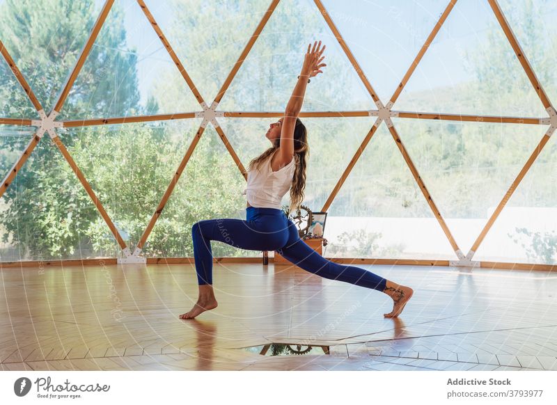 Anonymous woman standing in Crescent Lunge pose on floor crescent lunge yoga balance flexible barefoot vitality wellness arms raised window tattoo wooden