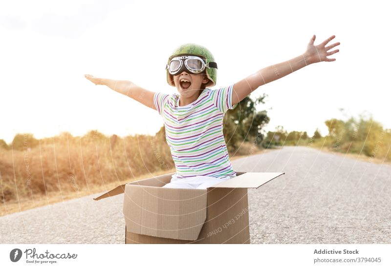 Excited boy in goggles sitting in cardboard box on road - a