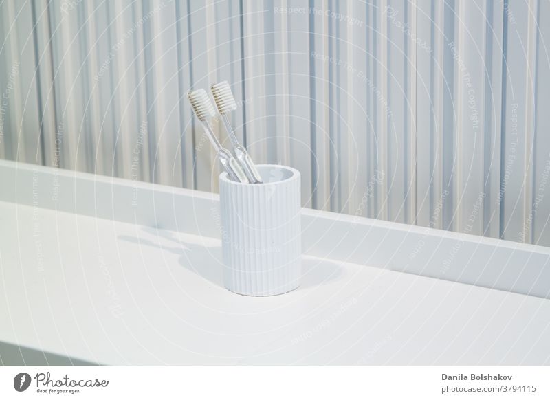two toothbrushes in white white cup in bathroom on striped background dental equipment daily toothbrush holder caries routine luxury clinic protection