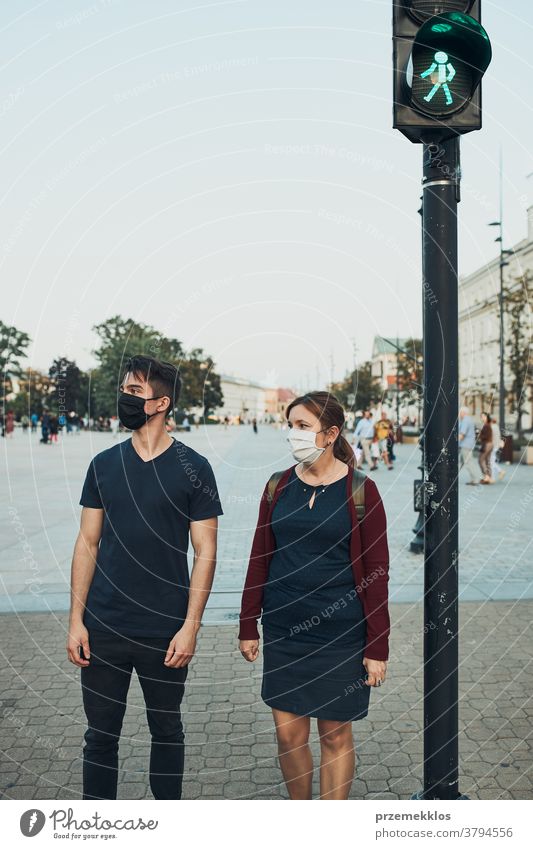 Man and woman waiting at pedestrian crossing next to traffic lights wearing the face masks to avoid virus infection and to prevent the spread of disease in time of coronavirus