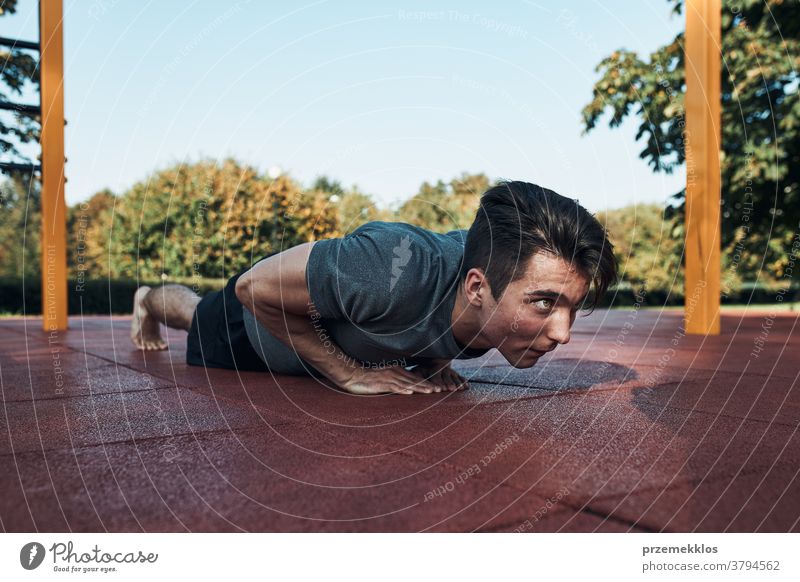 Young man doing push-ups on a red rubber ground during his workout in a modern calisthenics street workout park care caucasian health lifestyle male one