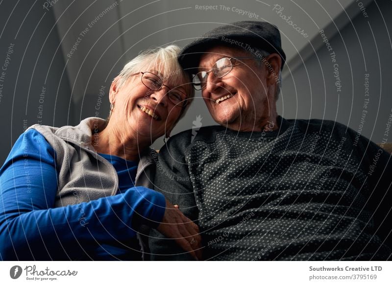 Laughing Senior Couple Sitting On Sofa At Home Watching Television Together couple senior seniors retired at home watching tv television sitting sofa together