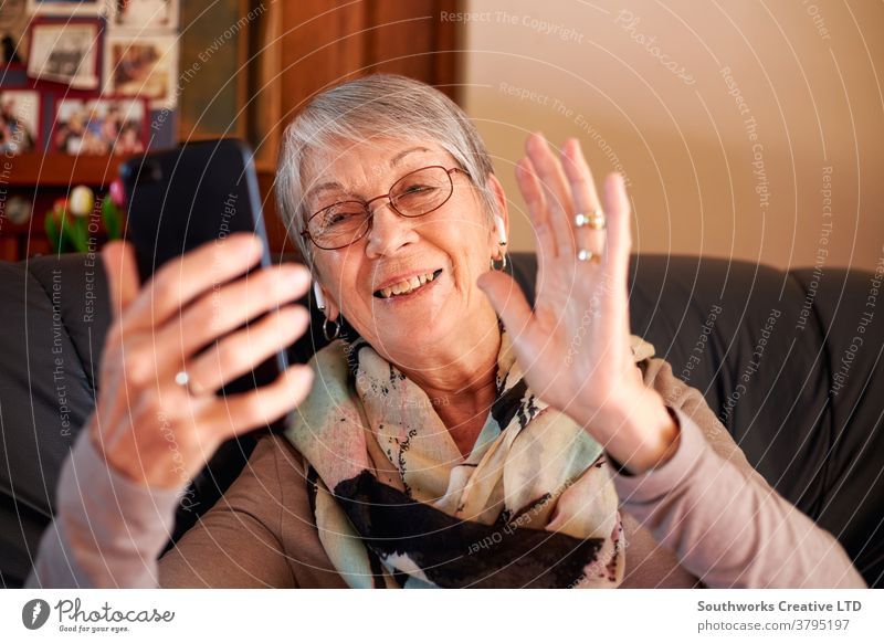 Smiling Senior Woman At Home Waving As She Makes Video Call To Family On Mobile Phone senior woman video call video chat mobile seniors cell at home