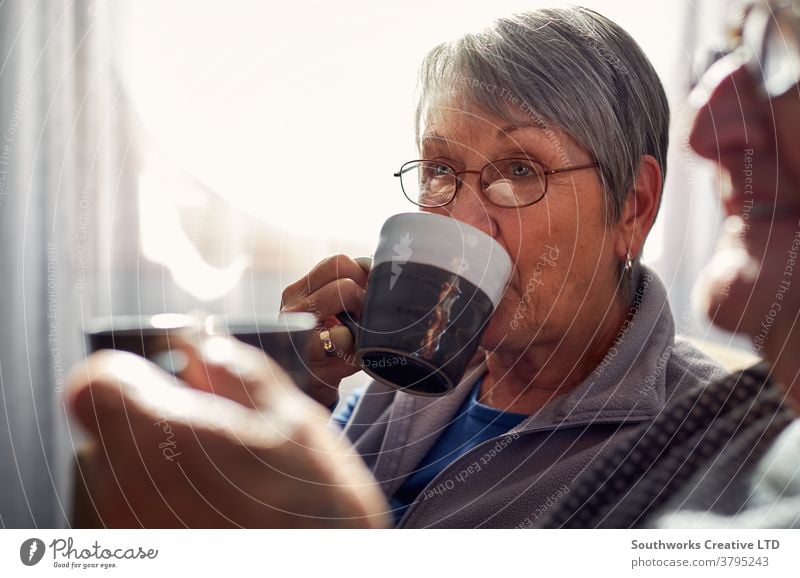 Senior Couple Relaxing And Chatting On Sofa At Home Together With Hot Drink couple senior seniors retired at home relaxing sitting sofa talking chatting drink