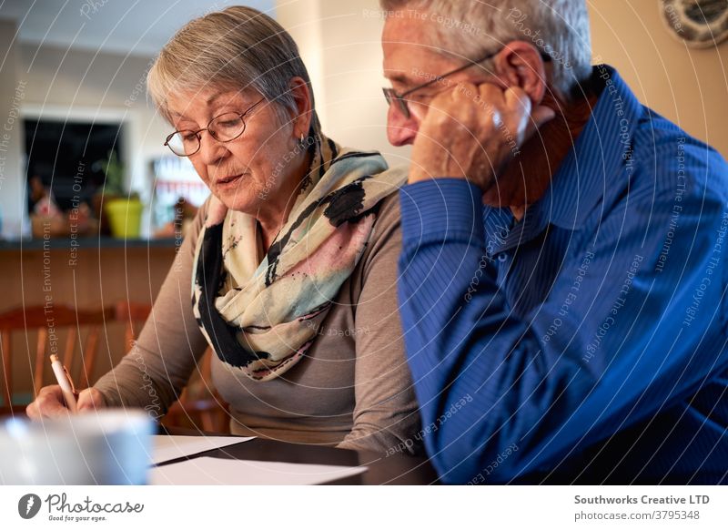 Senior Couple At Home Sitting At Table Checking Personal Finances couple senior seniors retired at home shopping buying choosing checking holiday finance