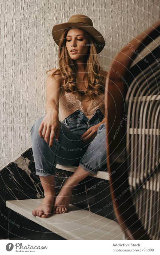 Stylish woman sitting on stairs in house casual style hat jeans appearance outfit charming relax staircase female stairway wooden modern step vacation tranquil