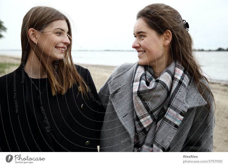 Portrait of two young women - friends - on the beach of the Elbe Woman Young woman 18-25 years warmly pretty Charming Slim Brunette long hairs Fresh Large smart