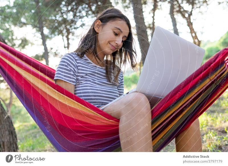 Smiling woman in hammock with laptop freelance project using typing startup independent cheerful female young internet gadget device netbook browsing lying work