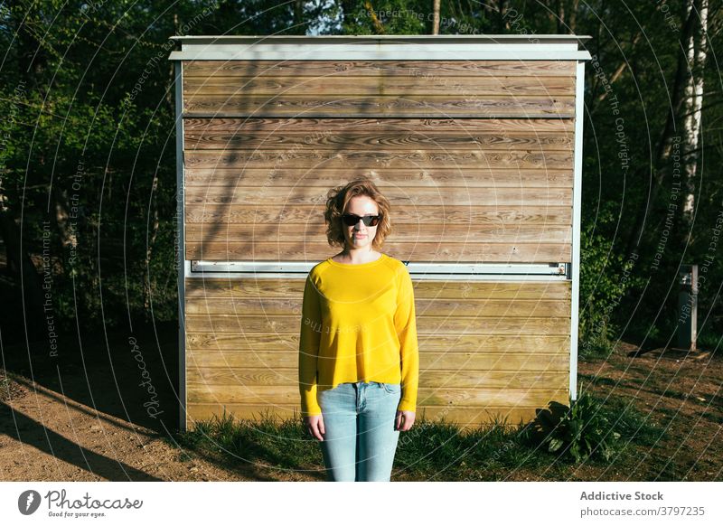 Stylish woman in yellow outfit in park style trendy fashion sunlight color vivid sunglasses female content smile wooden building relax modern stand charming