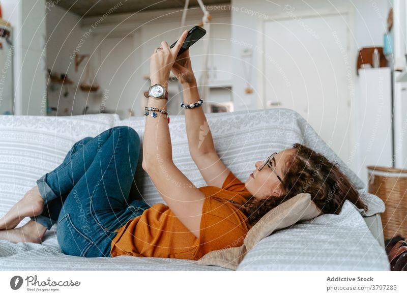 Young female taking self portrait on smartphone lying on sofa woman selfie relax social media comfort using gadget home device lazy young casual ginger hair