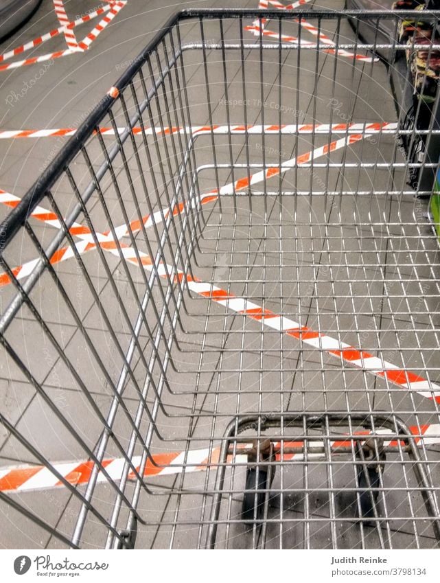 Empty shopping trolley in the checkout area with umpteen barrier strips stuck to the floor | Corona | Everyday life during the pandemic|
