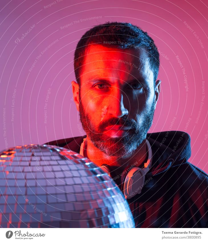 Colorful studio portrait of a bearded deejay with headphones against red and blues background. disco music colored pop sound disco ball mirrors clubbing