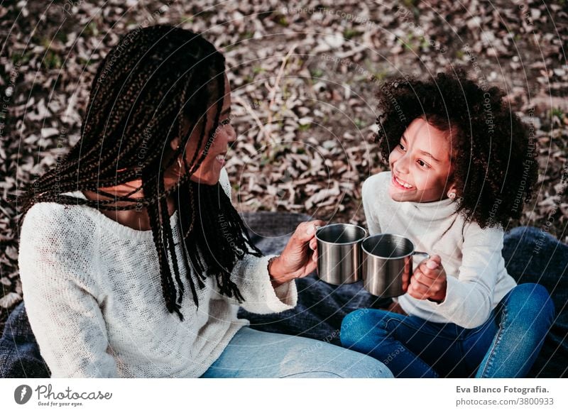 hispanic mother and afro kid girl doing picnic outdoors relaxing in nature. Autumn season. Family concept portrait daughter family mixed race motherhood