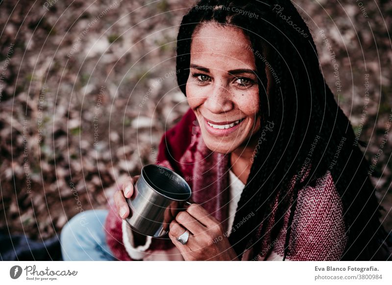 hispanic mid adult woman outdoors holding a mug of water. Autumn season afro woman latin portrait sunset nature hat smile happy joy young happiness people