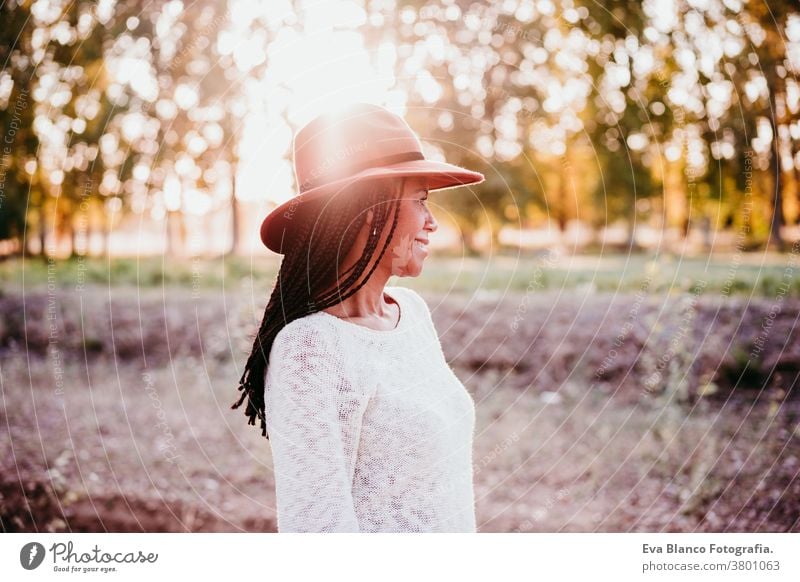 portrait of mid adult hispanic woman wearing a hat at sunset during golden hour, autumn season afro woman latin nature outdoors smile happy joy young happiness