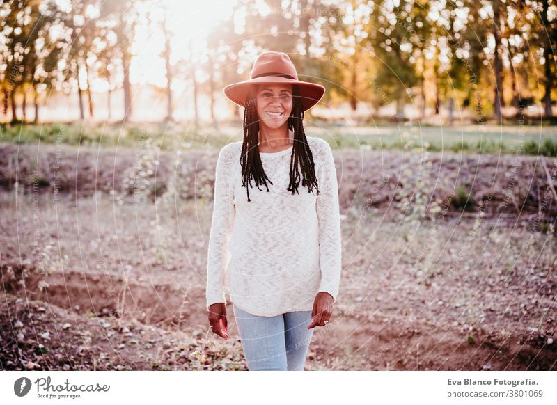 portrait of mid adult hispanic woman wearing a hat at sunset during golden hour, autumn season afro woman latin nature outdoors smile happy joy young happiness