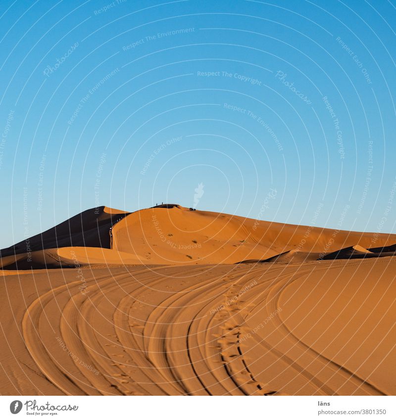 Arabian man in blue clothes walking on a desert dune. - a Royalty