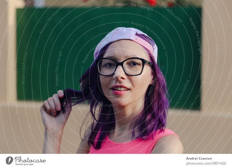 Young purple haired Caucasian Woman looking at the camera and playing with her hair, wearing pink cap and shirt 30s adult attractive beautiful blouse casual