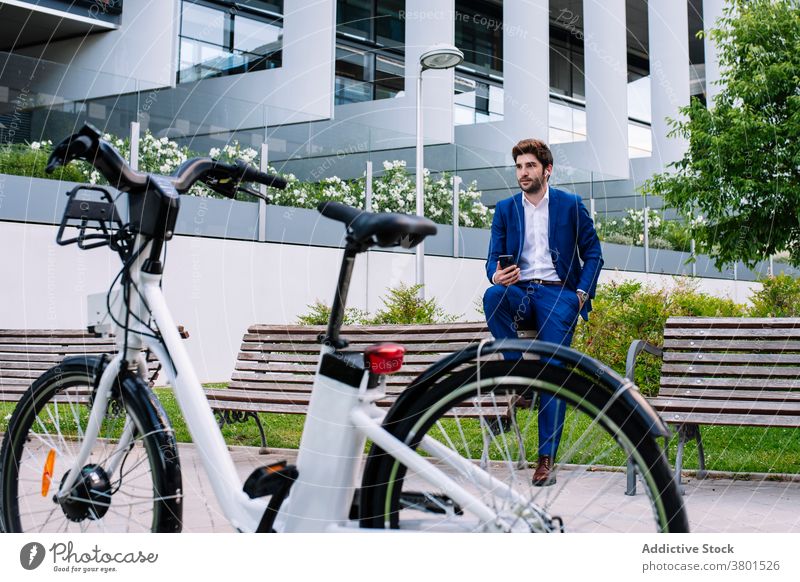 Stylish entrepreneur in formal suit looking at wristwatch on bench businessman stylish electric bike town masculine handsome device bicycle city building