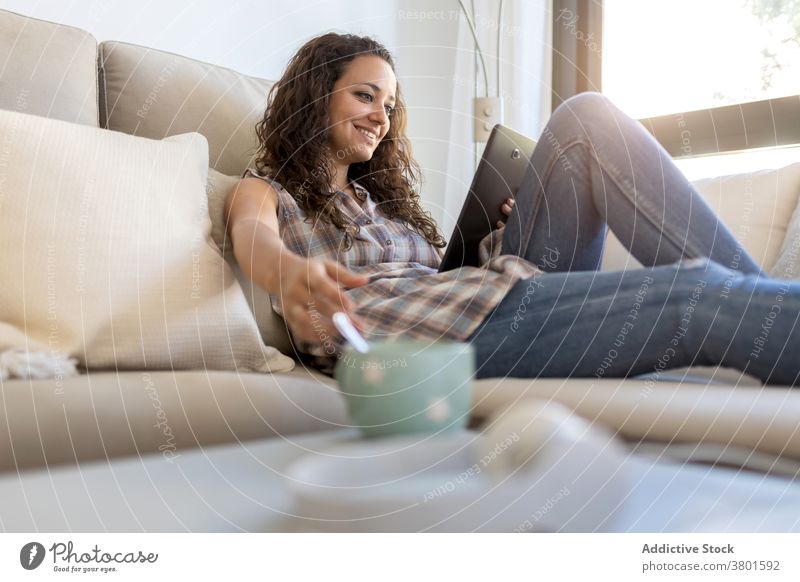 Cheerful woman browsing tablet in living room relax home entertain using message domestic weekend female internet connection social media happy device sofa
