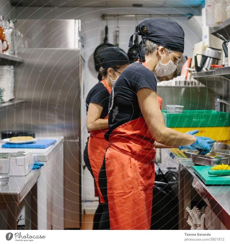 Cooks in a restaurant protected by a mask as a precaution against the coronavirus preparing takeaway food. cook kitchen salad covid-19 chef vegetarian cooking