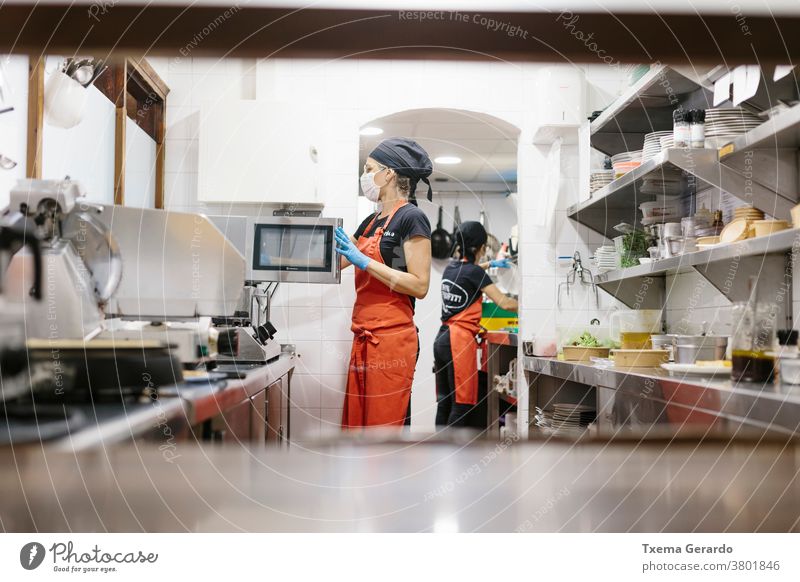 Cooks in a restaurant protected by a mask as a precaution against the coronavirus preparing takeaway food. The containers used are compostable. cook kitchen