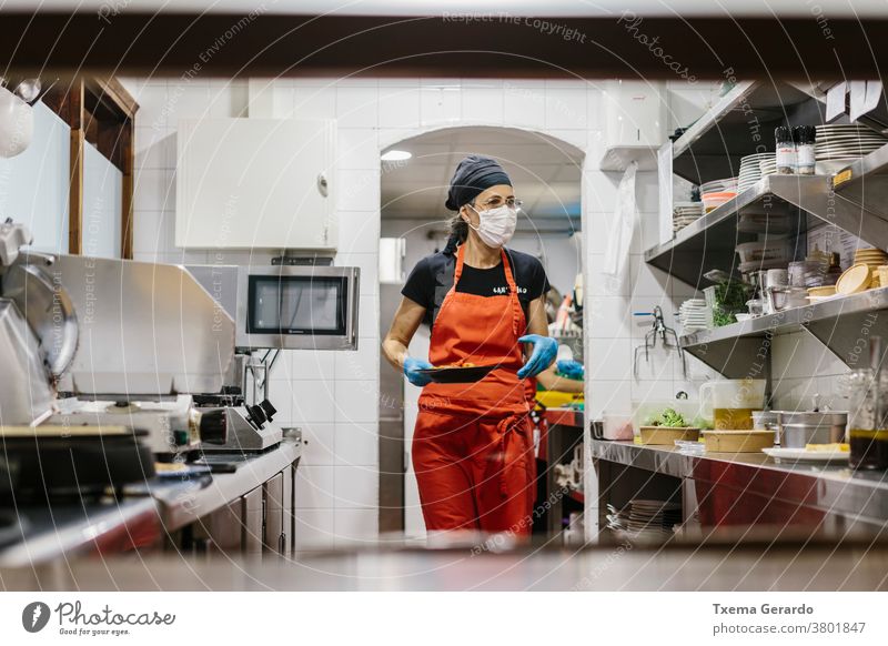 Cooks in a restaurant protected by a mask as a precaution against the coronavirus preparing takeaway food. The containers used are compostable. cook kitchen