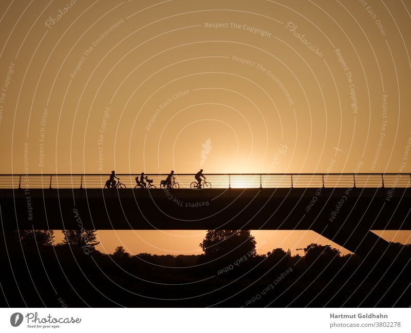 Silhouetten einer Gruppe Fahrradfahrer die kurz vor Sonnenuntergang über eine Brücke fahren. Ausflug Bauwerk Fahrad fahren Fahren Fahrräder Fahrzeug Familie