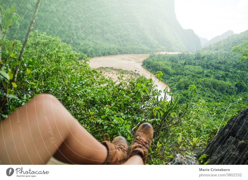 A hiker's legs resting on a ledge overlooking the river and lush forest in Nong Khiaw village in Luang Prabang, Laos Nong Kiaw hiking view wanderlust travel